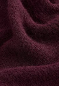 Burgundský pletený materiál s měkkou, chlupatou strukturou, s viditelnými vlákny a mírně otevřeným tkaním, vytvářející hloubku a teplo.