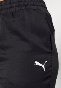 Shorts atletici neri in tessuto liscio, con cintura elastica e un logo bianco di un puma che salta sul lato.