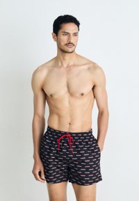 Sorinți negre de înot cu un model repetat de logo-uri albe și roșii, cu un tiv reglabil roșu și un design lejer.
