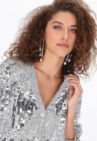 Szary kardigan z cekinami w serek, o miękkiej fakturze i dekoracyjnych guzikach. Ozdobiony błyszczącymi, odblaskowymi cekinami.