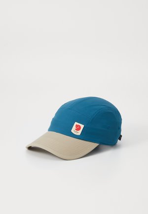 Blue fabric cap with a beige visor, featuring a red logo label on the front and stitching details. Suitable for outdoor activities.