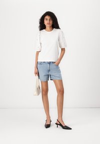 Vit kortärmad t-shirt med puffärmar, blå denimshorts, svarta slingbackklackar och en liten beige handväska.