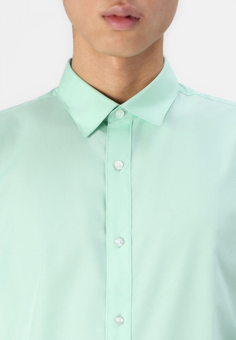 Camisa de manga larga color verde menta con cuello abotonado y pliegue delantero con botones blancos. Textura suave, tela ligera.