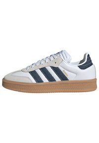 Fehér és tengerészkék sneaker, velúr és bőr anyagokból, három csíkkal, gumi talppal és párnázott gallérral a kényelem érdekében.