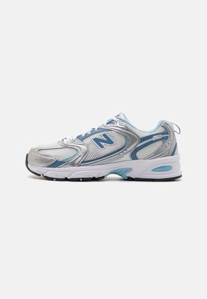 Silberne und hellblaue Sportschuhe mit einem Obermaterial aus Mesh, gebogener Sohlengestaltung, gepolstertem Schaft und "N"-Logo an der Seite. Mit sichtbaren Nähten als Akzent.
