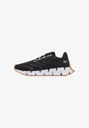 Baskets noires d'athlétisme avec côtés texturés ondulés, semelle blanche épaisse et segmentée, semelle extérieure couleur gomme, et logo Reebok sur le talon.