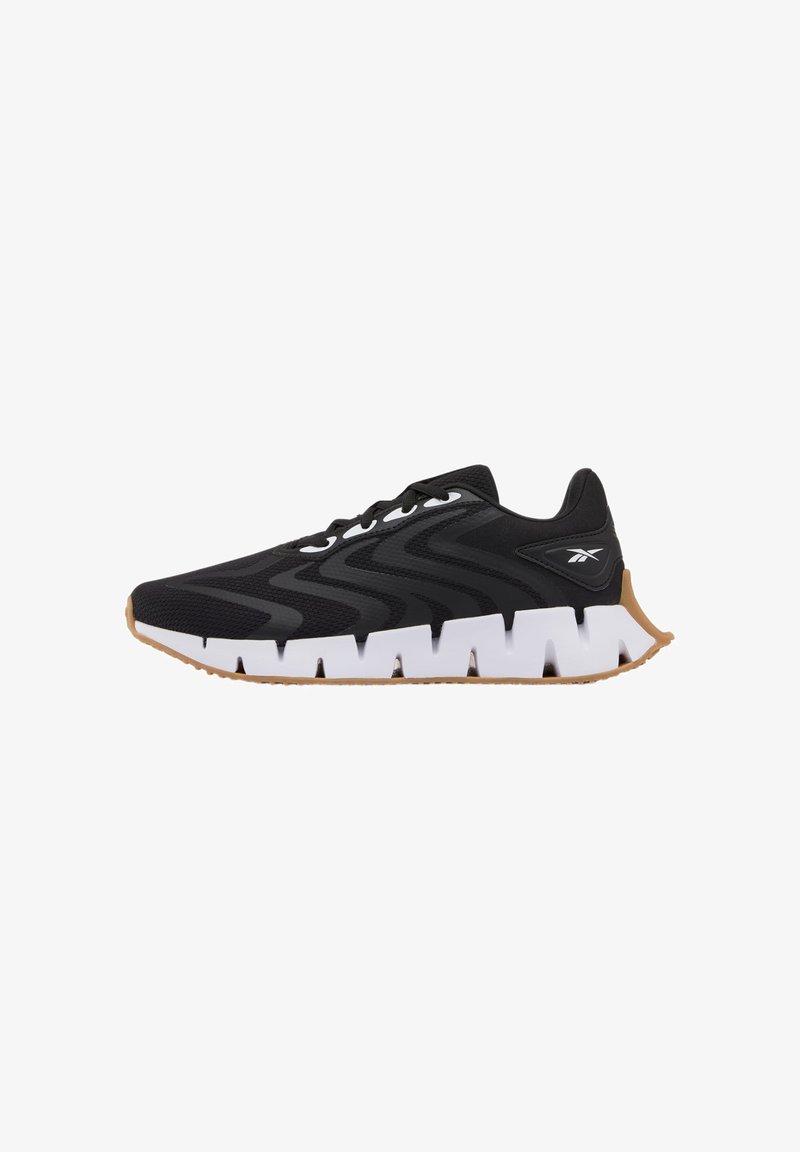 Baskets noires d'athlétisme avec côtés texturés ondulés, semelle blanche épaisse et segmentée, semelle extérieure couleur gomme, et logo Reebok sur le talon.