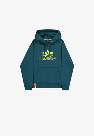 Teal hoodie with a kangaroo pocket, yellow "Alpha Industries" logo, drawstring hood, and red brand tag on the hem. Soft fabric.