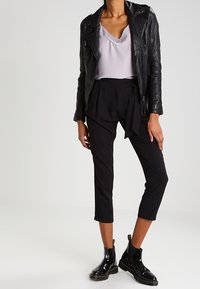 Svart läderbikerjacka över en ljuslila topp, ihop med svarta avklippta byxor och glänsande svarta ank stövlar med gyllene detaljer.