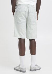 Svetlo zelene kratke hlače z elastičnim pasom, dvema velikima zadnjima žepoma z našitimi detajli, kombinirane s sivimi supergami in belimi nogavicami.