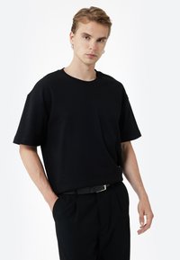 Czarna bawełniana koszulka z krótkim rękawem, okrągłym dekoltem i luźnym krojem, w zestawieniu z czarnymi spodniami i cienkim paskiem. Prosty design.