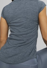 Mörkgrå idrottströja med korta ärmar, tillverkad av ett texturerat, lätt material. Har en rundad fåll och sömmar vid axlarna.