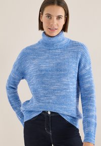 Pull à col roulé tricoté bleu clair avec une texture côtelée, doté de manches longues et d'une coupe décontractée. Le motif présente des petites taches blanches subtiles.