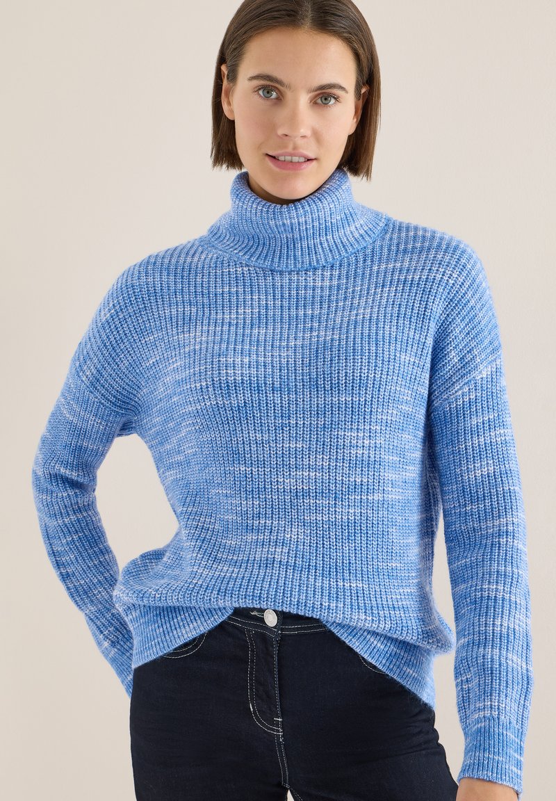 Pull à col roulé tricoté bleu clair avec une texture côtelée, doté de manches longues et d'une coupe décontractée. Le motif présente des petites taches blanches subtiles.