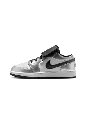 Baskets basses argentées et blanches avec le swoosh Nike noir, lacets noirs et une bride noire sur la languette sur fond blanc.