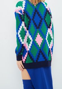 Knit sweater with geometric pattern in green, blue, pink, and white. Features long sleeves, ribbed cuffs, and side slit.