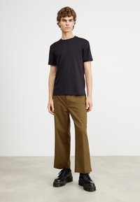 Sort t-shirt med korte ærmer og et lille brystlogo, parret med tanfarvede vide bukser og sorte chunky snørebåndsstøvler. Neutral baggrund.