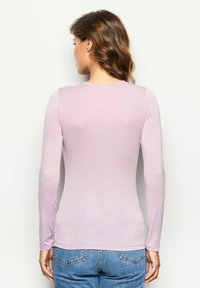 Langærmet top i lys lavendel, med rund hals og en glat, tætsiddende tekstur, parret med højtaljede denimjeans.