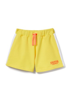 Pantaloncini con vita elastica gialla con strisce laterali bianche, coulisse rosa e piccolo logo arancione "Stranger Things" sulla gamba sinistra.