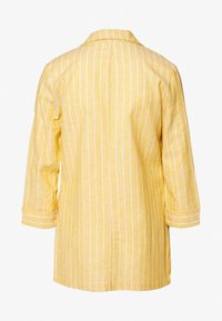 Żółta koszula w paski z rękawami do łokcia, kołnierzykiem, lekkim materiałem i prostym dołem. Posiada pionowe białe paski.