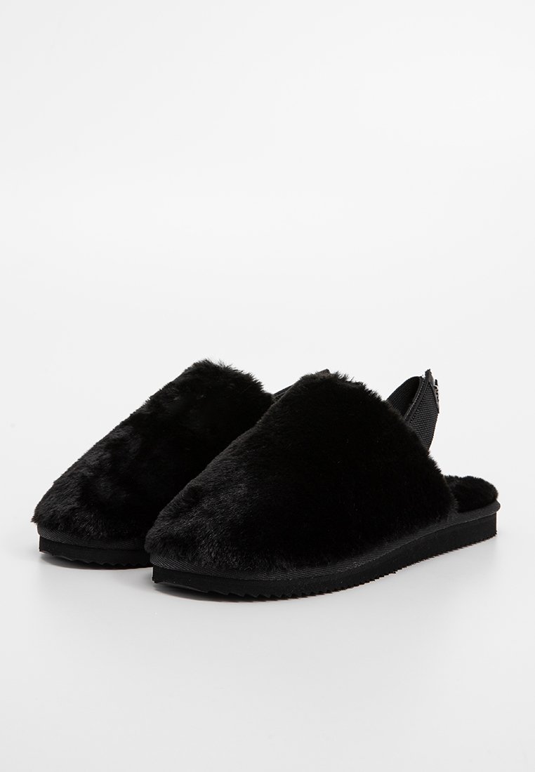 Zwarte instapslippers van zacht kunstbont, met een open achterkant. De zool is plat en van textuurrubber voor grip.