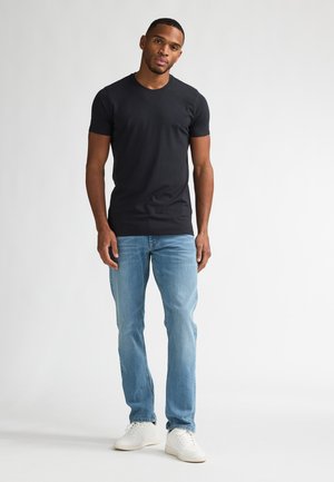 Zwart T-shirt met korte mouwen op een persoon, gecombineerd met lichtblauwe spijkerbroek en witte sneakers. Het shirt is glad, nauwsluitend en heeft een ronde hals.