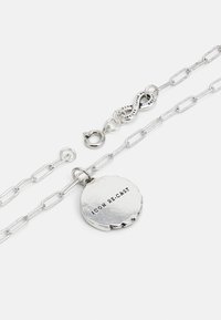 Bracelet en chaîne argentée avec des maillons allongés, comportant un pendentif rond gravé "ICON RE-CAST" et un fermoir avec un détail en symbole d'infini.