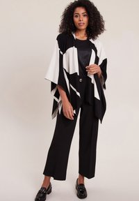 Zwart-wit gestructureerde poncho met een losse pasvorm, voorzien van een driehoekig ontwerp. Draag het over een zwart topje en combineer het met zwarte wijde broek en loafers.