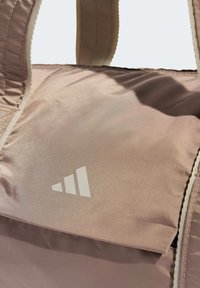 Sac de sport rose clair en matériau lisse et brillant, orné d'un logo blanc avec trois triangles empilés et de poignées robustes en sangle.