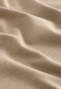 Béžová tkanina s měkkou texturou, vykazující přirozené záhyby a vrstvený vzhled. Materiál má jemný, konzistentní vzor.