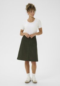 Groene corduroy rok met zakken, A-lijn vorm, en geschulpte witte geribbelde top. Gepaald met witte sokken en chunky sneakers.