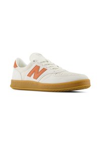 Zapatillas blancas con acentos naranjas, hechas de ante y cuero, que cuentan con una suela de goma texturizada y detalles perforados en la puntera.