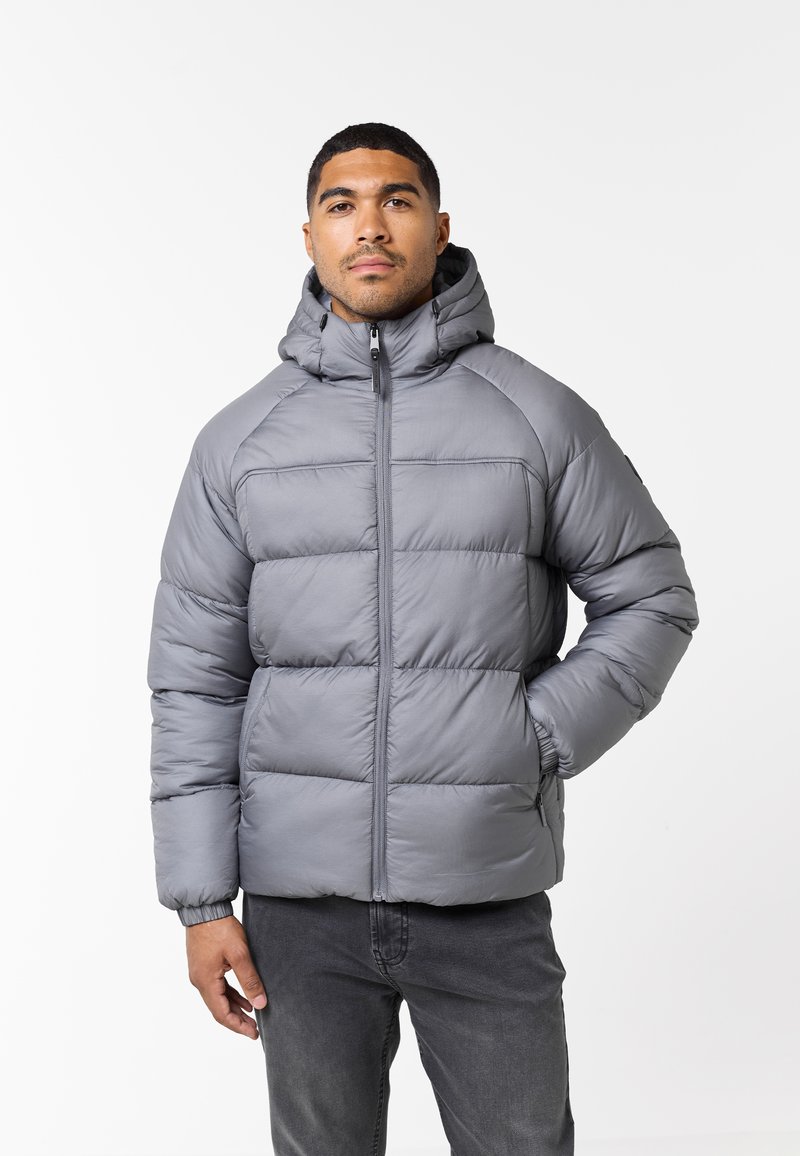 Chaqueta gris acolchada con capucha, que presenta secciones acolchadas y un cierre frontal. Puños elásticos y bolsillos laterales para mayor practicidad.