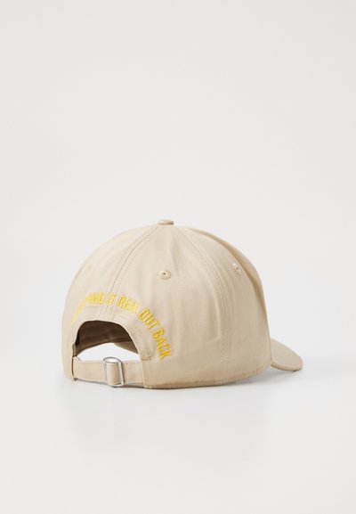 Casquette de baseball kaki avec une sangle en métal réglable et un texte brodé jaune à l'arrière indiquant "RESTER AUTHENTIQUE À L'ARRIÈRE."