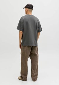 T-shirt gris surdimensionné à manches courtes, col rond, associé à un pantalon large marron clair et une casquette foncée. Design simple et décontracté.