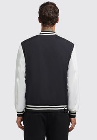 Zwart-wit bomberjack met een satijnen afwerking, gestreepte ribboorden en een gladde textuur. Kenmerkt zich door een effen zwarte achterkant.