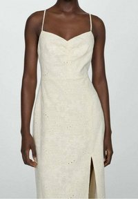 Robe sans manches couleur crème avec un col en cœur, une broderie florale et une fente latérale. Fabriquée dans un tissu léger et texturé.