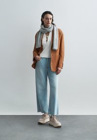 Smeđi antilop sako preko bijele pamučne majice s rebrastim uzorkom, svijetloplave traperice širokih nogavica, siva šal i bež masivne tenisice s smeđim đonom.