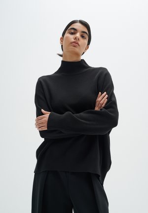 Black knit turtleneck sweater with long sleeves, relaxed fit, and ribbed cuffs. Smooth texture, minimalistic design. Paired with black trousers.