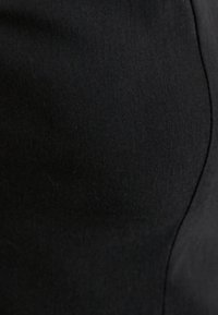 Schwarzer, elastischer Stoff mit einer glatten Textur, der ein eng anliegendes Design und subtile Nähte aufweist und so ein schlankes, stromlinienförmiges Erscheinungsbild erzeugt.