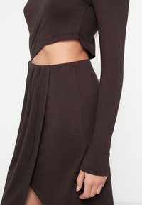Hnedý dlhý rukáv krátky top s oblým lemom, skombinovaný so zodpovedajúcou sukňou s rozparkom. Mäkká, textúrovaná látka s priliehavým strihom.