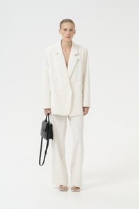 Bílý pruhovaný oblekový blazer a ladící kalhoty, doplněné černou kabelkou. Model nosí sandály s otevřenou špičkou. Hladká textilie.