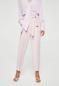 Lichtroze op maat gemaakte broek met een hoge taille, riemdetail en een taps toelopende fit. Gecombineerd met een lavendelkleurige blouse met lange mouwen en witte sandalen.