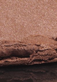 Brązowa, teksturowana powierzchnia o połyskującym wykończeniu, z lekko nierówną krawędzią i warstwową, miękką kompozycją.