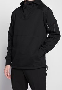 Černý kapucňový pulover vyrobený z jemné tkaniny; má poloviční zip vpředu, boční kapsy a texturované ramenní panely s tažným lemem.