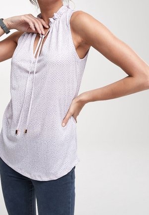 Sleeveless light lavender blouse with textured pattern and tie neckline worn by person with one hand on hip and other adjusting collar.