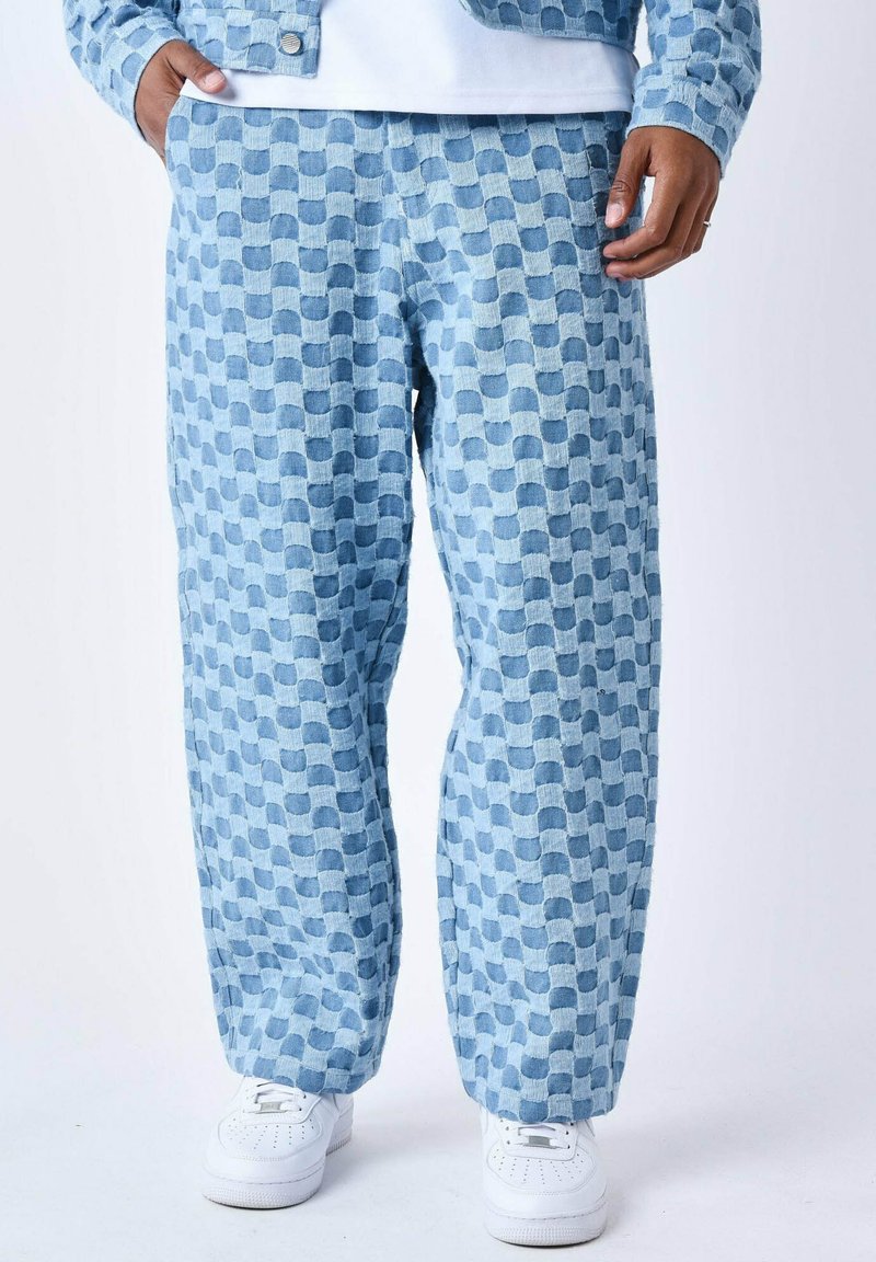 Pantaloni in corduroy azzurri chiari con un motivo geometrico testurizzato, dotati di vestibilità ampia e tasche laterali, abbinati a sneakers bianche.