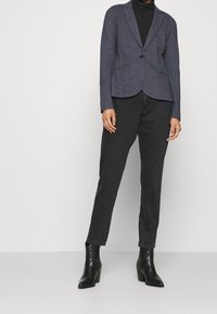 Tmavě námořnický dokonale střižený blazer s jednořadovým zapínáním, klopovými límci a vypolstrovanými rameny, doplněný o černé rovné džíny a boty na podpatku.