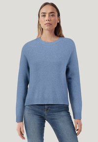 Hellblauer Pullover aus strukturiertem Strickstoff. Mit einem gerippten Ausschnitt und Saum, langen Ärmeln und einer lockeren Passform. Kombiniert mit Jeans.