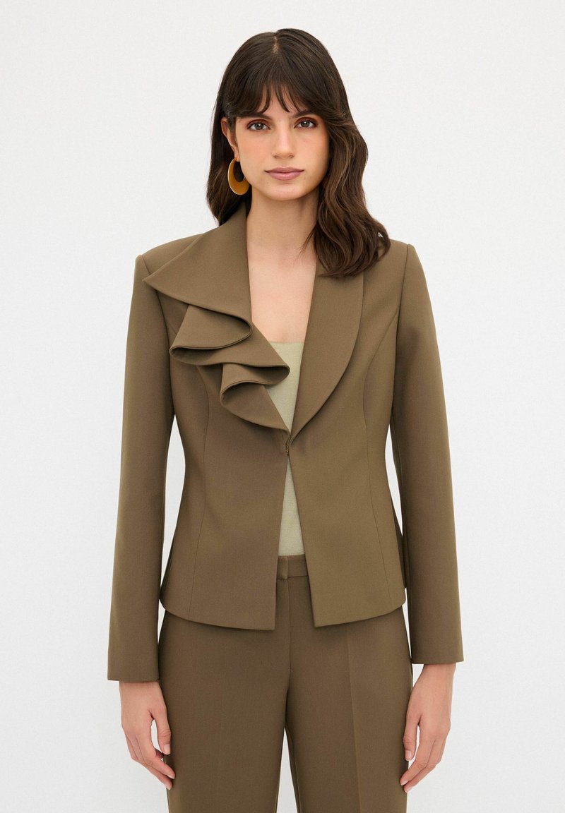 Blazer verde oliva con un ampio colletto arricciato, design aderente, maniche lunghe e chiusura con un singolo bottone. Tessuto dalla texture liscia.